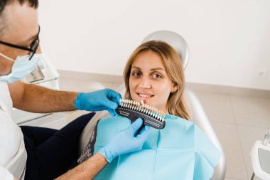 Diş beyazlatma. Diş hekimi, diş tonu rehberiyle çalışıyor. Diş hekimliği. Doktor diş sağlığı kliniğinde diş rengine uyan örnekleri kontrol ediyor.