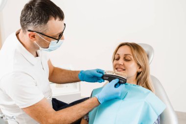 Diş beyazlatma. Diş hekimi, diş tonu rehberiyle çalışıyor. Diş hekimliği. Doktor diş sağlığı kliniğinde diş rengine uyan örnekleri kontrol ediyor.