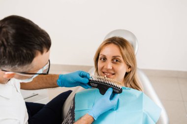 Diş beyazlatma. Diş hekimi, diş tonu rehberiyle çalışıyor. Diş hekimliği. Doktor diş sağlığı kliniğinde diş rengine uyan örnekleri kontrol ediyor.