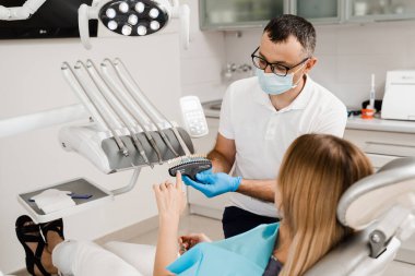 Diş hekimi, diş sağlığı kliniğindeki kadın hastalara diş beyazlatma için diş tonu rehberliği gösteriyor. Diş hekimliği. Kadın kaplamalara bakıyor ya da diş implantı yerleştiriyor. Diş renkleri doktorun ellerinde eşleşiyor.