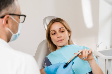 Diş beyazlatma konusunda dişçiye danışmak ve dişçi kliniğinde dişçi dişlerinin rengini göstermek. Diş hekimliği. Kadın diş rengine bakıyor. Doktorun ellerindeki örneklerle eşleşiyor.