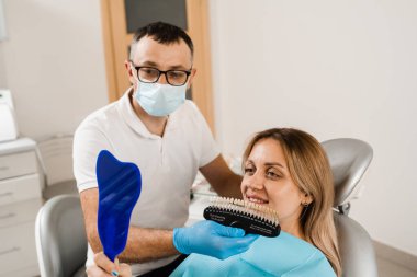 Diş beyazlatma. Hasta diş rengi gölgeler rehberine bakıyor. Diş hekimliği. Doktor diş sağlığı kliniğinde diş rengine uyan örnekleri kontrol ediyor.