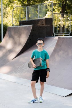 Happy young child boy with skate board on playground and smile. Extreme sport lifestyle. Smiling child with skate board posing on sport ramp