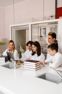 Discussion with a teacher at a chemistry lesson in a laboratory. Group of classmates are discussing chemistry experiments and homework at school. Education concept