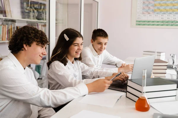 Chemistry lesson in labaratory. Education online in class with group of pupils studying on laptop, smiling and having fun together