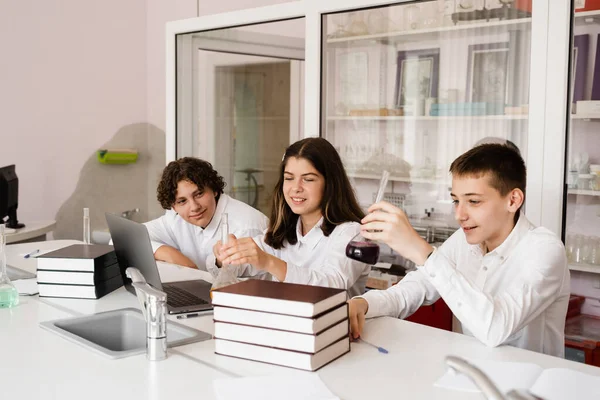 Pupils holding flasks with liquid for experiments in laboratory. Education concept. Group of pupils studying chemistry lesson in school