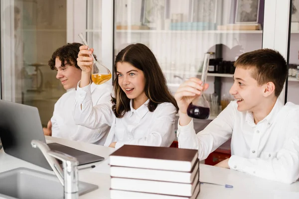 Pupils holding flasks with liquid for experiments in laboratory. Education concept. Group of pupils studying chemistry lesson in school