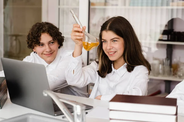Chemistry lesson. Schoolgirl and classmates holds flask for experiments and smiles in the laboratory. School education