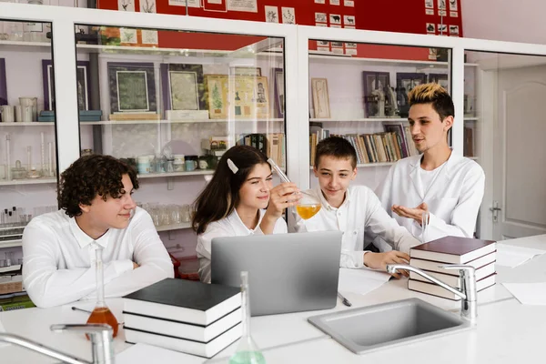 School teacher gives chemistry lesson to children in a laboratory with flasks with liquids for experiments. Education concept. Group lesson of classmates at chemistry lesson