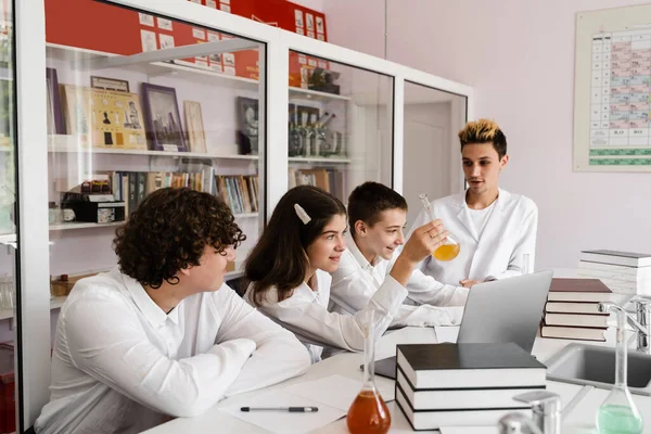 School teacher gives chemistry lesson to children in a laboratory with flasks with liquids for experiments. Education concept. Group lesson of classmates at chemistry lesson