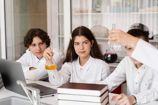 School teacher gives chemistry lesson to children in a laboratory with flasks with liquids for experiments. Education concept. Group lesson of classmates at chemistry lesson