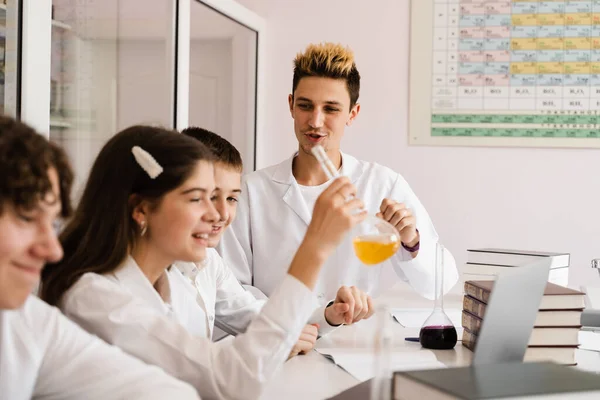 School chemistry teacher shows children flasks with liquids for experiments in the laboratory. Education concept. Group lesson of classmates at chemistry lesson