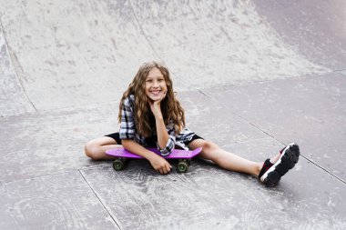 Kaykay parkında spor rampasında oturan çekici çocuk. Kuru tahtayla poz veren aktif bir genç. Aşırı yaşam tarzı.