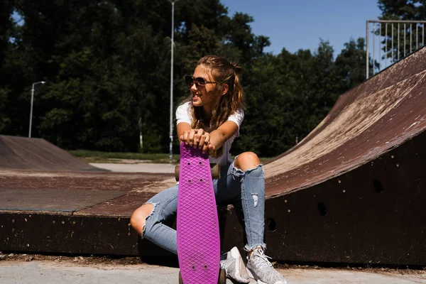 Happy smiling girl with skate board sitting on skate playground and having fun. Extreme sport lifestyle. Laughing child with skate board posing on sport ramp