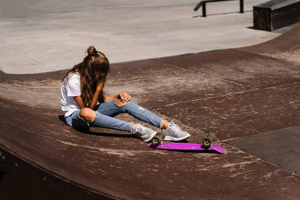 Active child girl after fall from penny board injured, sitting and feel pain on sport ramp on skate park playground