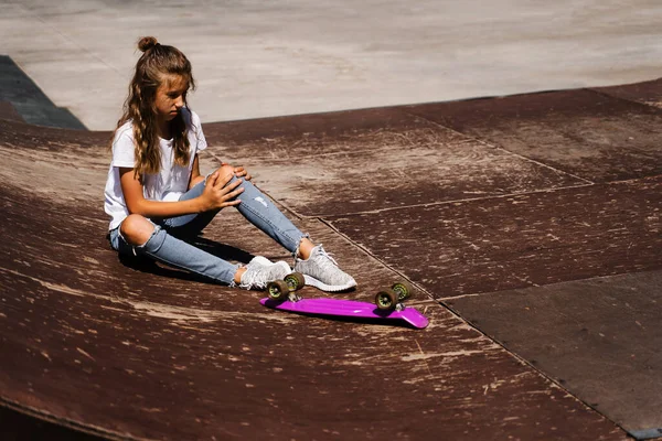 Active child girl after fall from penny board injured, sitting and feel pain on sport ramp on skate park playground