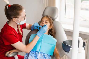 Pediatric dentist examines teeth of child girl for treatment of toothache. Pain in teeth in children. Consultation with pediatric dentist in dentistry
