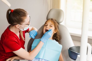Pediatrik dişçi diş ağrısı tedavisi için çocuk kızın dişlerini muayene ediyor. Çocuklarda diş ağrısı. Diş hekimliğinde pediatrik dişçiye danışmanlık