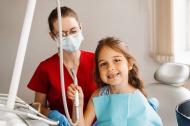 Neşeli kız çocuğu diş matkabı tutuyor ve dişçilikte gülümsüyor. Çocuk konsültasyonda dişçiye gülümsüyor.