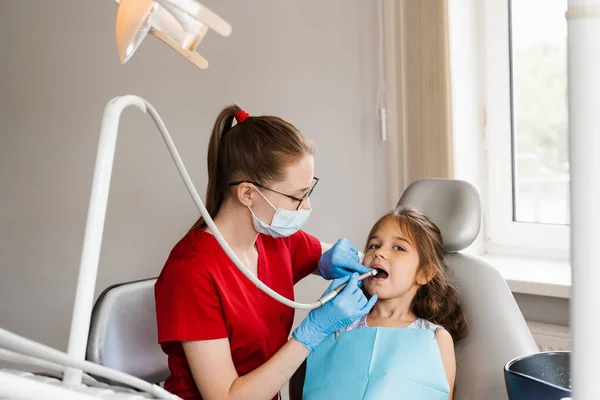 Child dentist with dental drill treats child girl in dentistry clinic. Dental filling for child patient