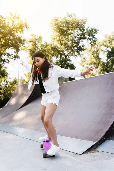 Shocked child girl before fall from penny board on skate park playground at sunset. Sports equipment for kids. Active teenager with pennyboard on skate park playground