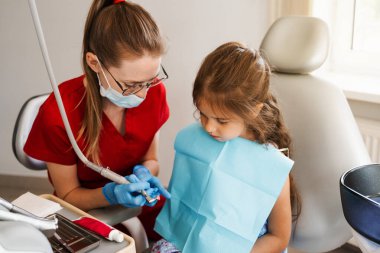 Professional hygiene for teeth of child in dentistry. Professional teeth cleaning for child girl. Pediatric dentist examines and consults kid patient in dentistry