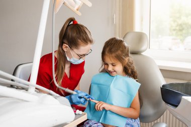 Professional hygiene for teeth of child in dentistry. Professional teeth cleaning for child girl. Pediatric dentist examines and consults kid patient in dentistry
