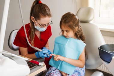 Professional hygiene for teeth of child in dentistry. Professional teeth cleaning for child girl. Pediatric dentist examines and consults kid patient in dentistry