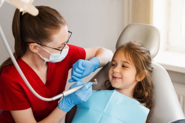 Professional hygiene for teeth of child in dentistry. Professional teeth cleaning for child girl. Pediatric dentist examines and consults kid patient in dentistry