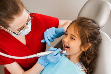 Child dentist makes professional teeth cleaning in dentistry. Professional hygiene for teeth of child in dentistry. Pediatric dentist examines and consults kid patient in dentistry