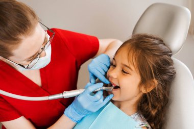 Child dentist makes professional teeth cleaning in dentistry. Professional hygiene for teeth of child in dentistry. Pediatric dentist examines and consults kid patient in dentistry