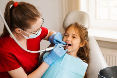 Pediatrik dişçi kız diş hekimliğinde profesyonel diş temizliği yapar. Diş hekimliğindeki çocuk dişleri için profesyonel hijyen. Pediatrik dişçi, diş hekimliğindeki çocuk hastalarını muayene eder ve muayene eder.