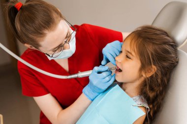 Child dentist makes professional teeth cleaning in dentistry. Professional hygiene for teeth of child in dentistry. Pediatric dentist examines and consults kid patient in dentistry