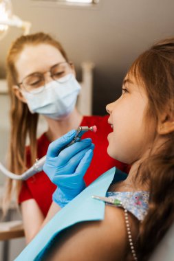 Professional teeth cleaning for child girl in dentistry. Professional hygiene for teeth of child. Pediatric dentist examines and consults kid patient in dentistry