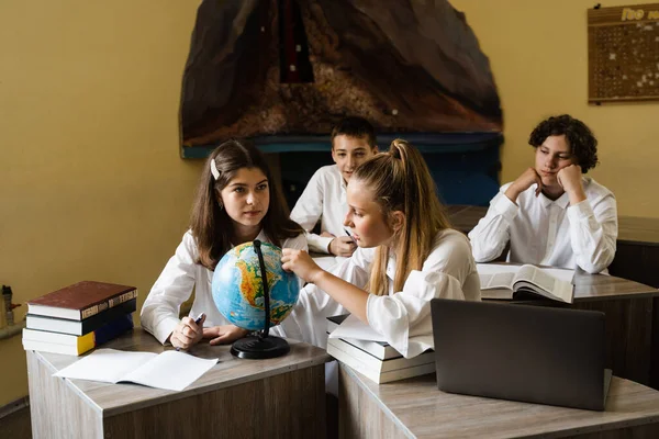 Children in geography lesson look at globe and discuss different countries. Education concept. Schoolchildren rotate globe and communicate with each other