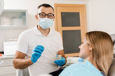 Dental prosthetics consultation with dentist for patient woman in dentistry. Doctor dentist shows artificial plastic jaw with dental implants