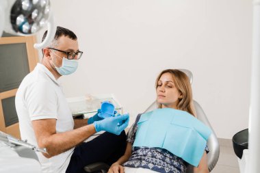 Dentist show mouth guard for teeth whitening in dentistry. Doctor orthodontist consult woman patient about home teeth whitening procedure