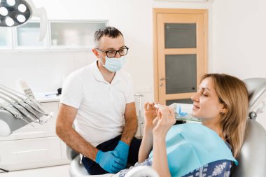 Clear aligner for bite correction and shape of teeth. Orthodontist shows transparent removable retainer for patient woman in dentistry