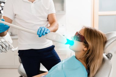 UV teeth whitening for woman patient in protective glasses in dentistry. Laser bleaching teeth in clinic. Dentist do ultraviolet whitening of teeth