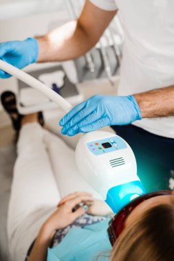 UV teeth whitening for woman patient in protective glasses in dentistry. Laser bleaching teeth in clinic. Dentist do ultraviolet whitening of teeth