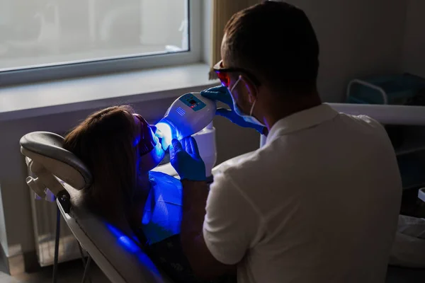 UV teeth whitening for woman patient in protective glasses in dentistry. Laser bleaching teeth in clinic. Dentist do ultraviolet whitening of teeth
