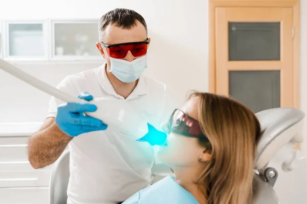 Artificial teeth whitening. Dental ultraviolet whitening treatment with light, fluoride and laser. Woman in red protective glasses patient do UV teeth whitening procedure