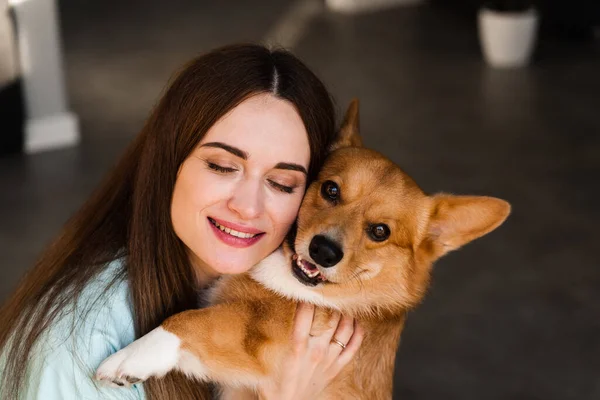 Domestic Corgi dog with girl owner. Young woman sitting on the floor and hug Welsh Corgi Pembroke. Lifestyle with domestic playful dog