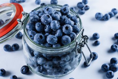 Blueberries with water drops in glass jar on white background. Blueberry summer seasonal berry. Many natural organic blueberries