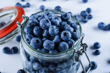 Blueberries with water drops in glass jar on white background. Blueberry summer seasonal berry. Many natural organic blueberries