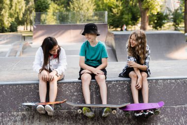 Kids friends with skateboard and penny boards posing on sport ramp on skate board park. Extreme lifestyle. Active children having fun together. Sports equipment