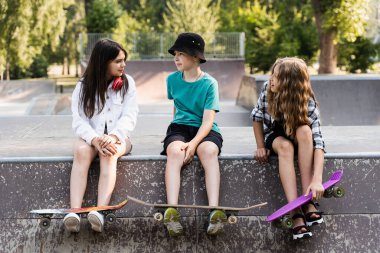 Kids friends with skateboard and penny boards posing on sport ramp on skate board park. Extreme lifestyle. Active children having fun together. Sports equipment