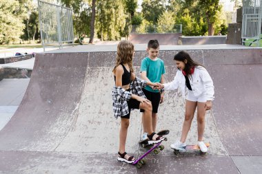 Kids friends with skateboards and penny boards stack their hands together and get ready for ride together on sport ramp on skate board playground. Concept of friendship sports support of children