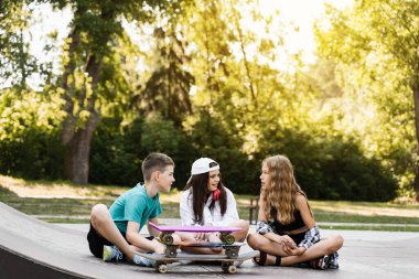 Fashion children with skateboard and penny boards communicate and discuss on the sports playground. Boy and girls friendship concept. Kids smile and laugh and have fun together