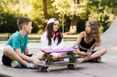 Kids smile and laugh and have fun together. Children with skateboard and penny boards communicate and discuss on the sports playground. Boy and girls friendship concept